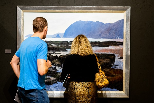 Two people standing looking at a Jurassic Coast painting at an art exhibition